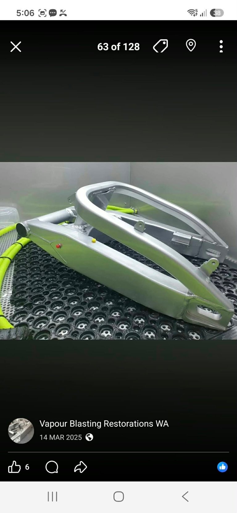 Large finished silver vapour-blasted frame inside the vapour blasting cabinet with black rubber mat and green hoses