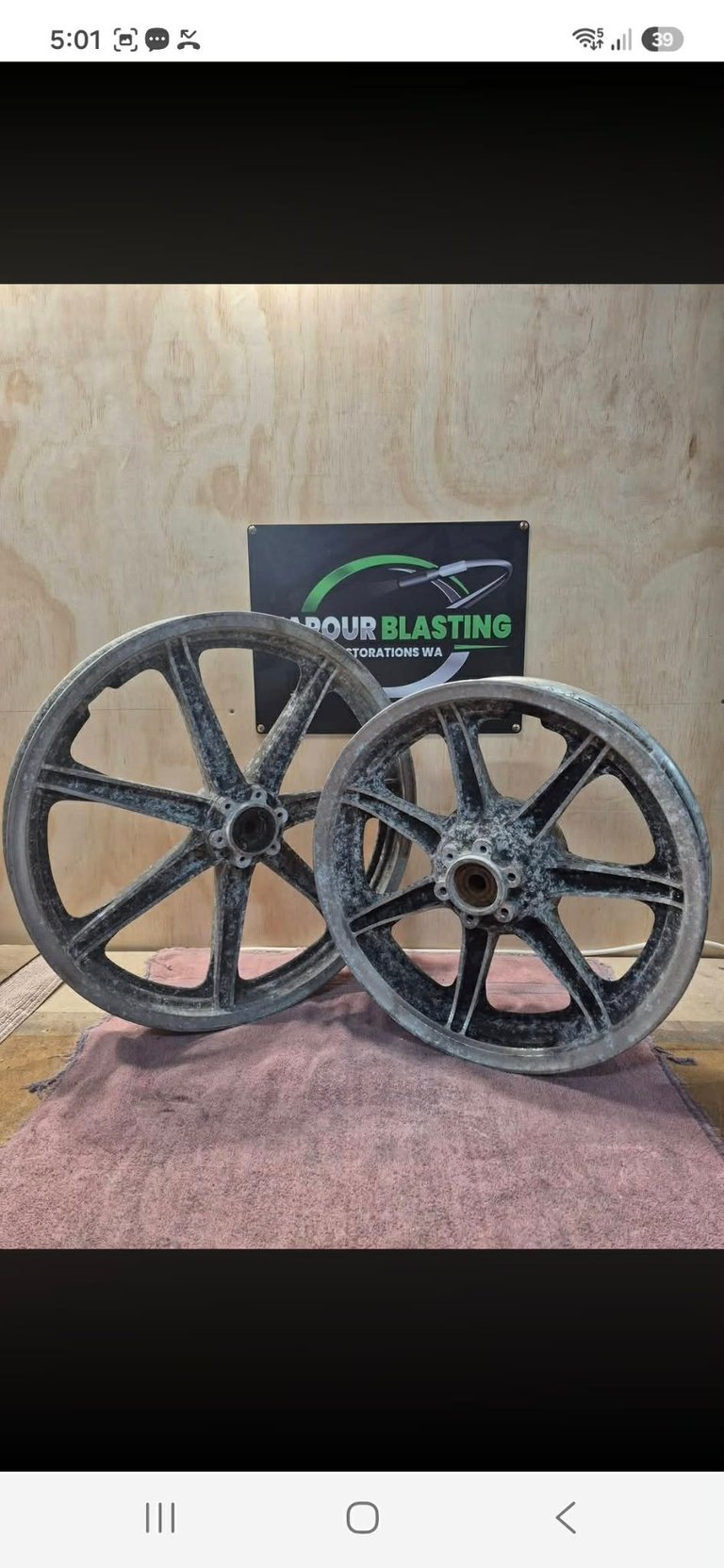 Two large cast iron industrial wheels displayed on a pink mat with a company logo sign in the background