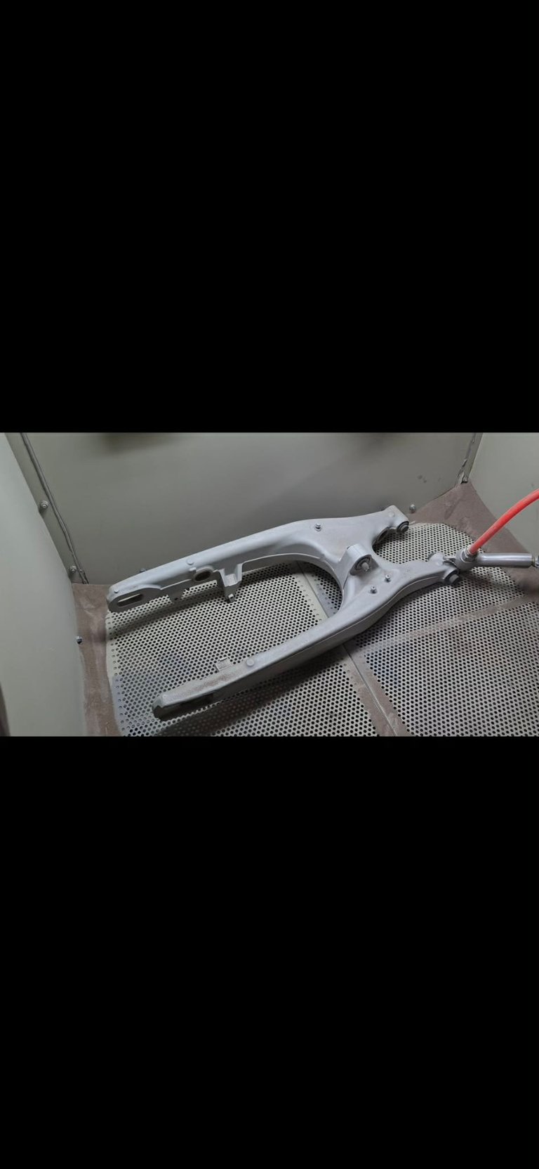 Dull matte grey component inside the dry blasting cabinet with perforated metal floor and red nozzle on the right